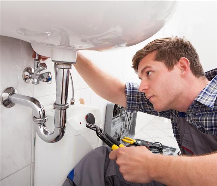 Image of a person performing maintenance on bathroom pipes. 